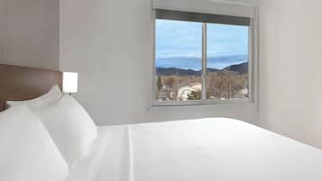 Habitación de hotel con una cama grande, cabecero y ventana con vista a las montañas.
