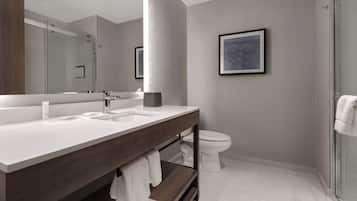 A modern bathroom with a large mirror, dual sinks, a toilet, and a shower area.