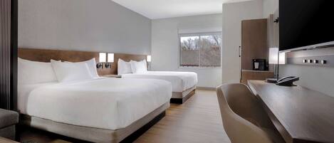 A hotel room with two beds, a desk, a chair, and a TV.