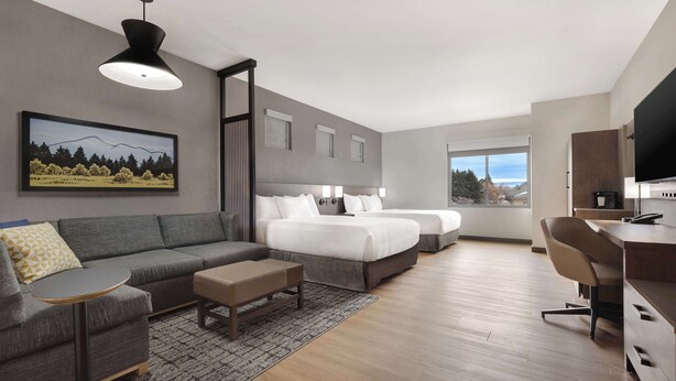 A modern hotel room with a grey sofa, two beds, a desk, and a large window offering a view of the outdoors. - Hyatt Place Flagstaff (Flagstaff)