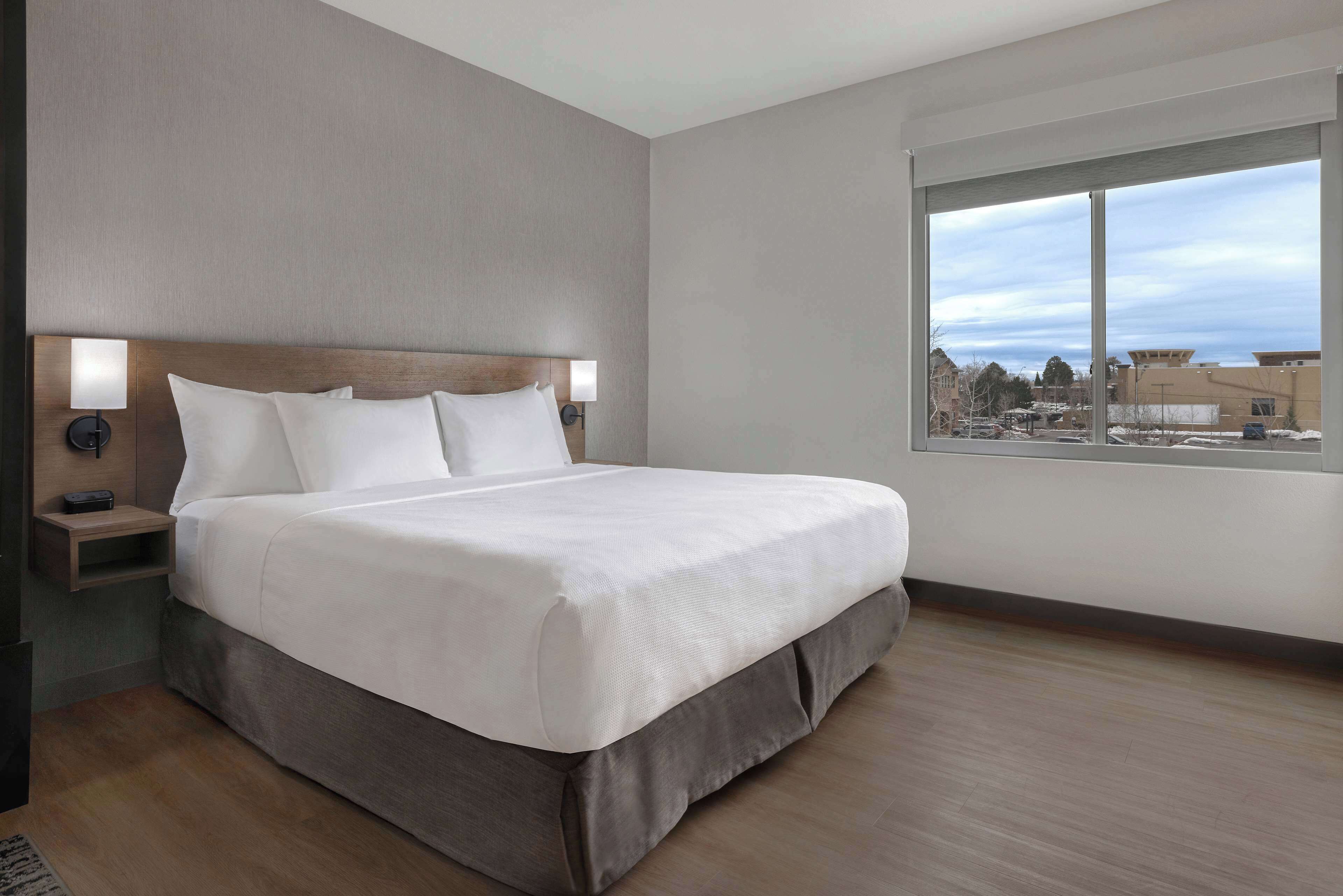 Una habitación de hotel moderna con una cama grande, una mesita de noche con lámpara y una ventana que ofrece vistas a la ciudad.
