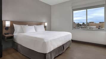 Una habitación de hotel moderna con una cama grande, una mesita de noche con lámpara y una ventana que ofrece vistas a la ciudad.