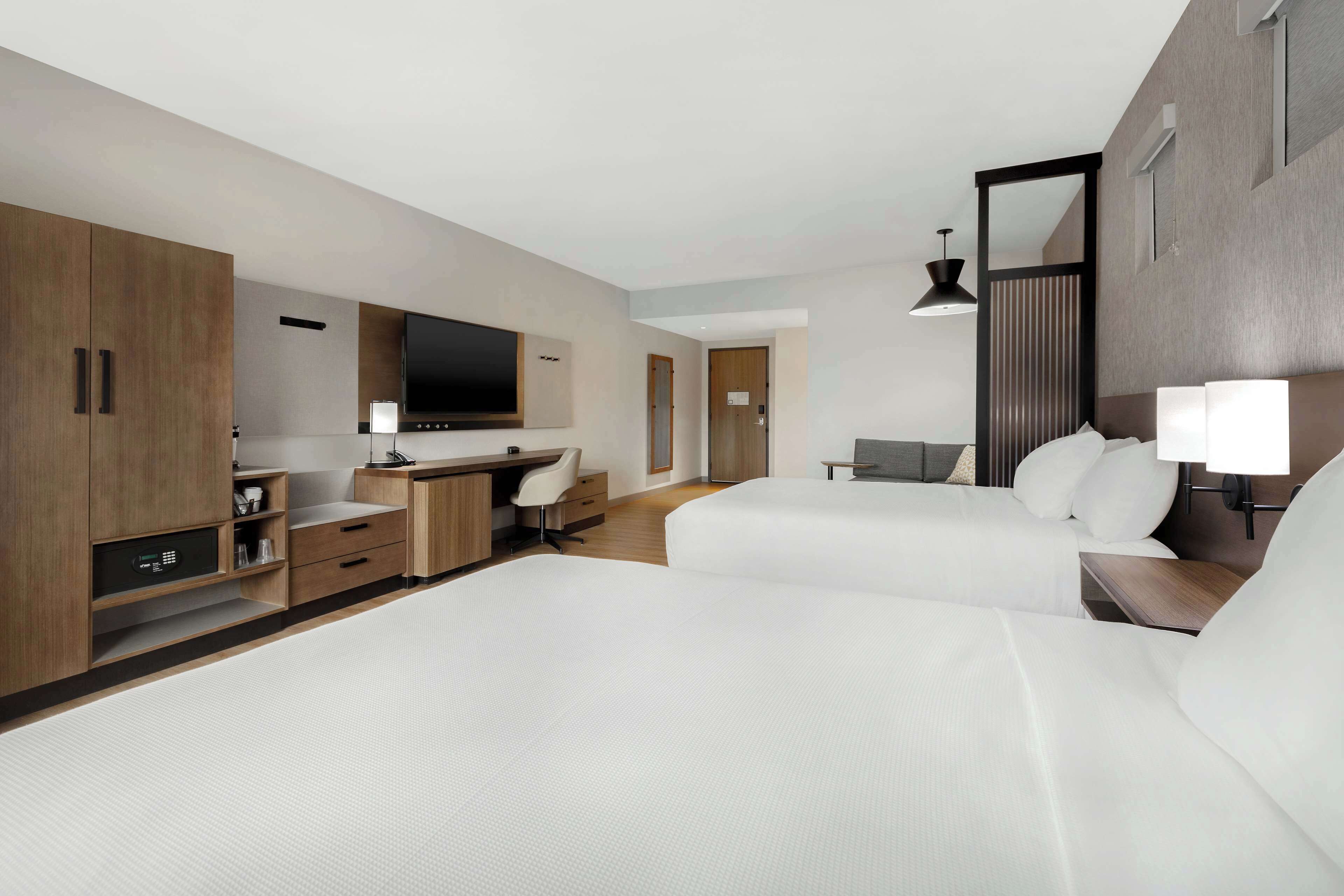 A modern hotel room with two beds, a desk, a TV, and a wardrobe.