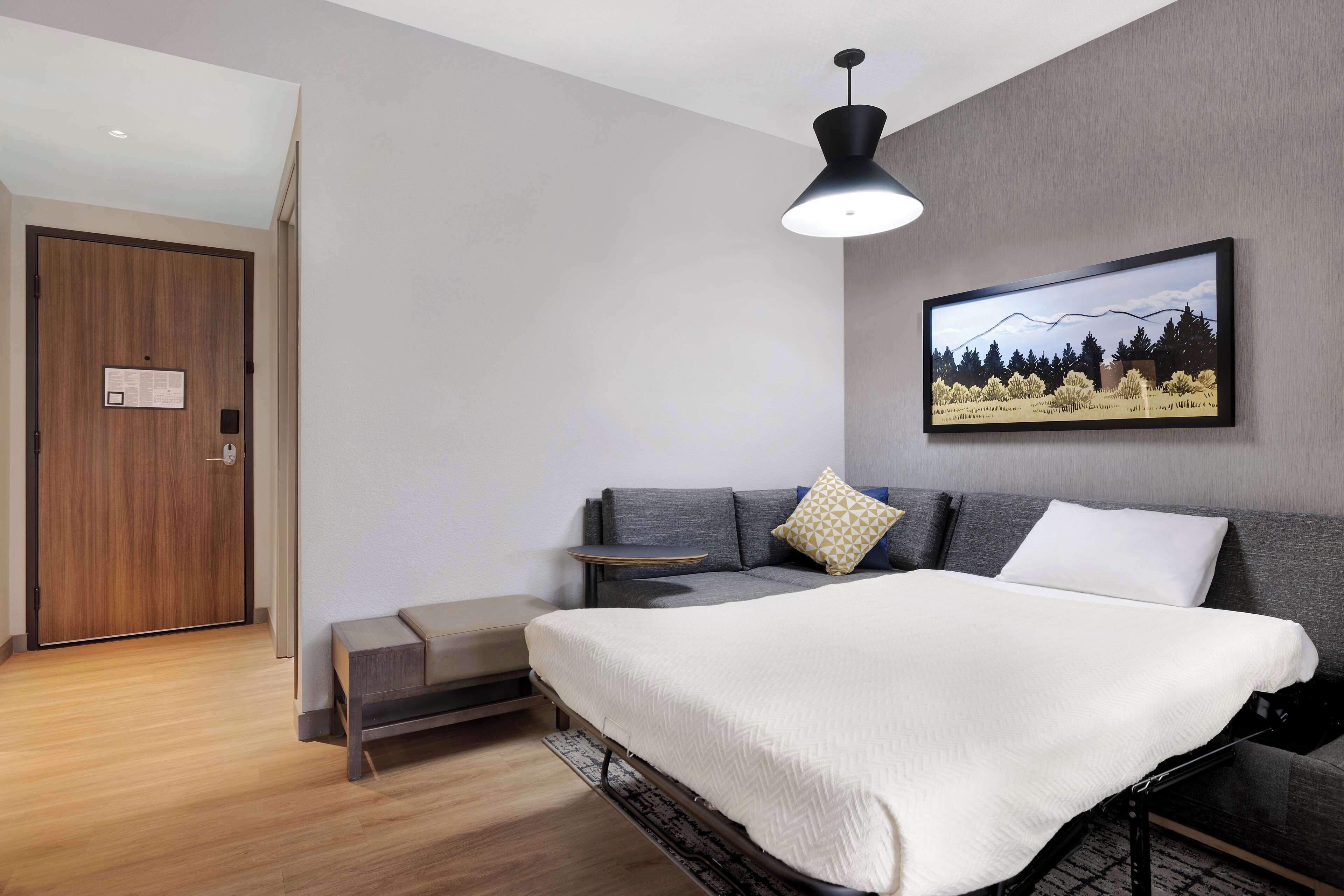 A modern bedroom with a bed, a sofa, a bench, a painting, and a door.