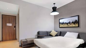 A modern bedroom with a bed, a sofa, a bench, a painting, and a door.