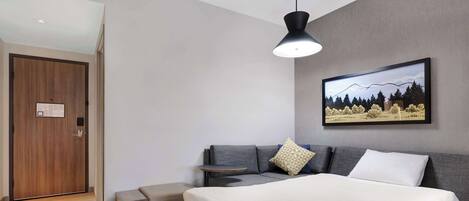 A modern bedroom with a bed, a sofa, a bench, a painting, and a door.