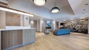 A modern reception area with a wooden reception desk, a blue seating area, and a large wall with a geometric pattern. - Hyatt Place Flagstaff (Flagstaff)