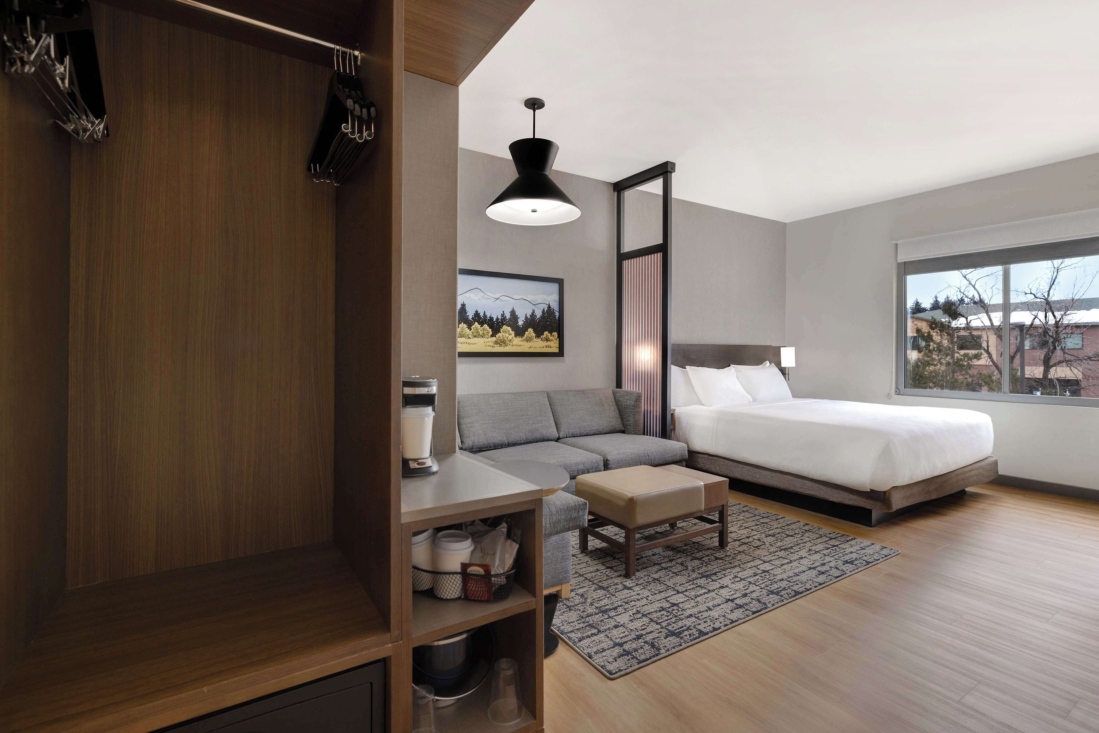 A modern bedroom with a bed, a gray sofa, a wooden wardrobe, a desk, and a large window.