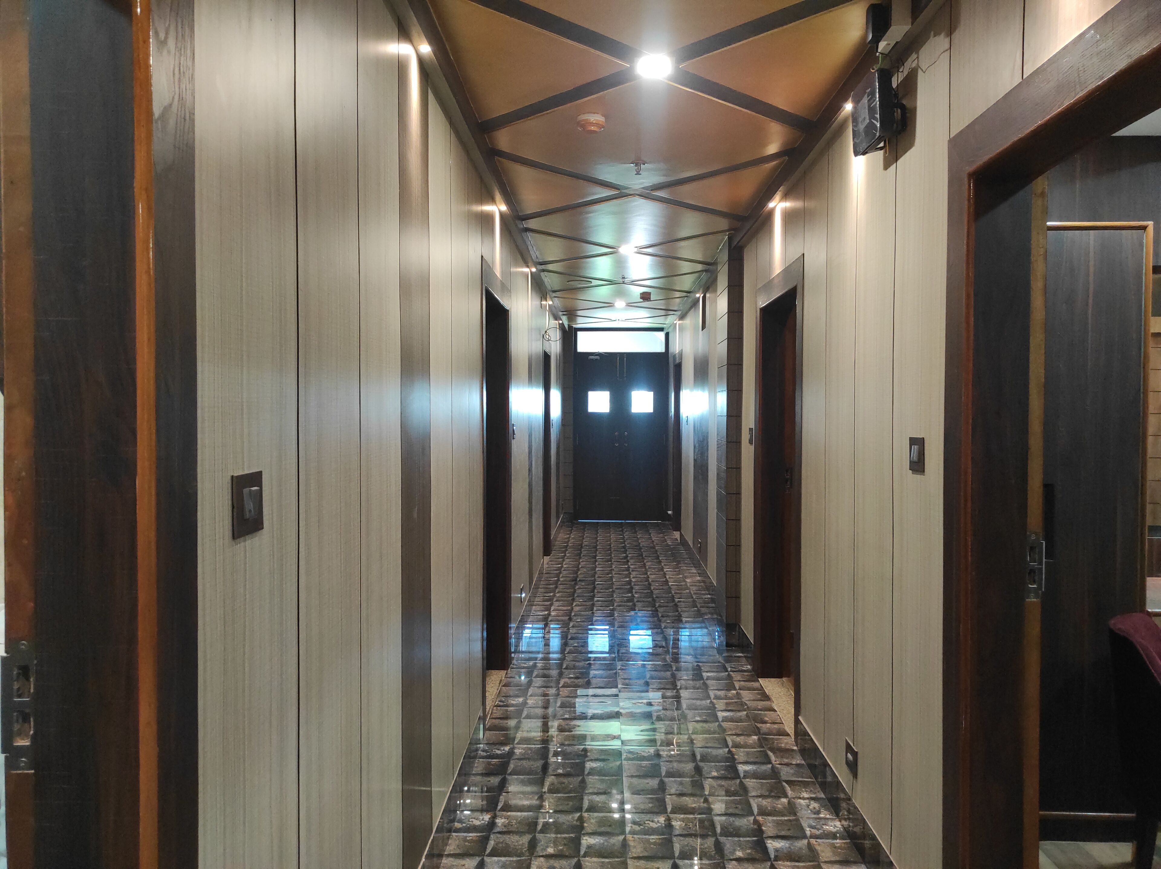 A hallway with a patterned floor, wooden doors, and a ceiling with exposed beams and lighting fixtures.