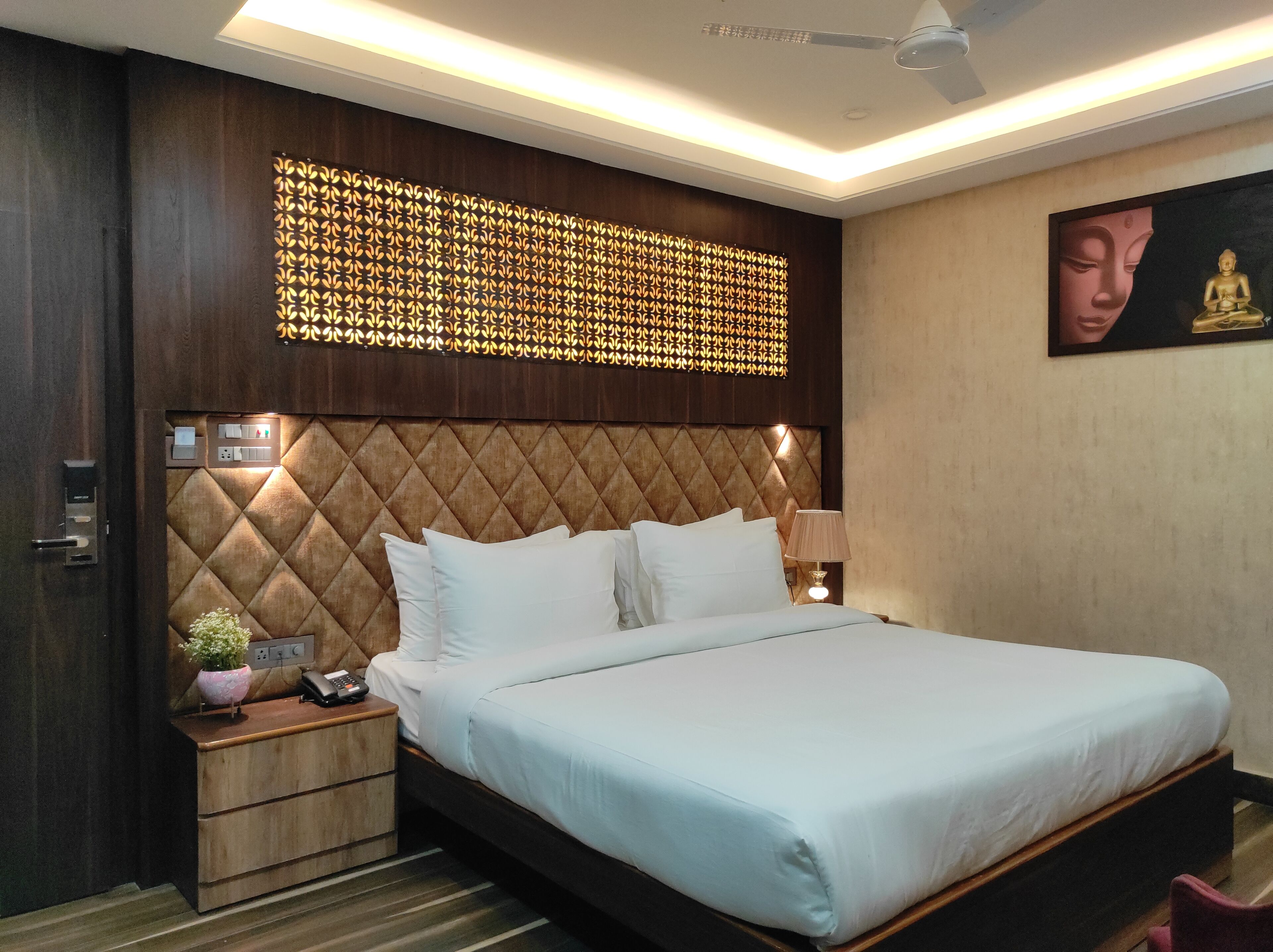 Une chambre d’hôtel avec un grand lit, une tête de lit en bois, un panneau décoratif, une table de chevet avec une lampe et un tableau au mur.