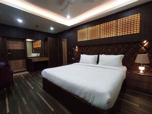A modern hotel room with a large bed, a wooden headboard, a mirror, a wardrobe, and a decorative light panel on the wall.