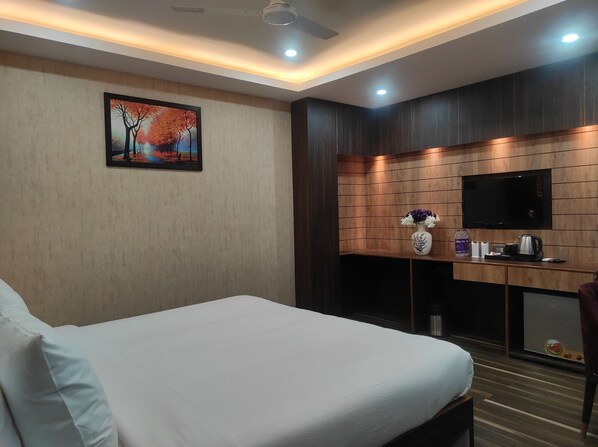 A hotel room with a bed, a desk with a TV, a painting, and a vase of flowers. - Hotel Aavas Inn (Tezpur)