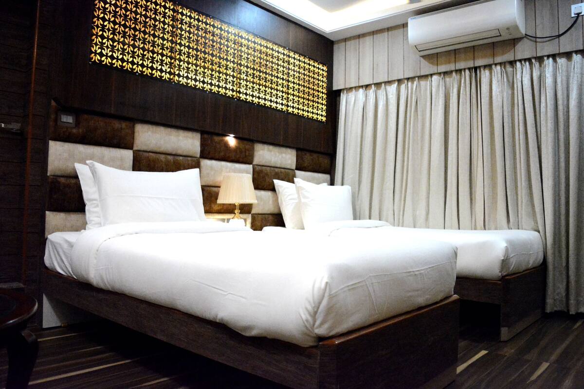 A hotel room with a large bed, a bedside table, a wall-mounted air conditioner, and a decorative wall panel.