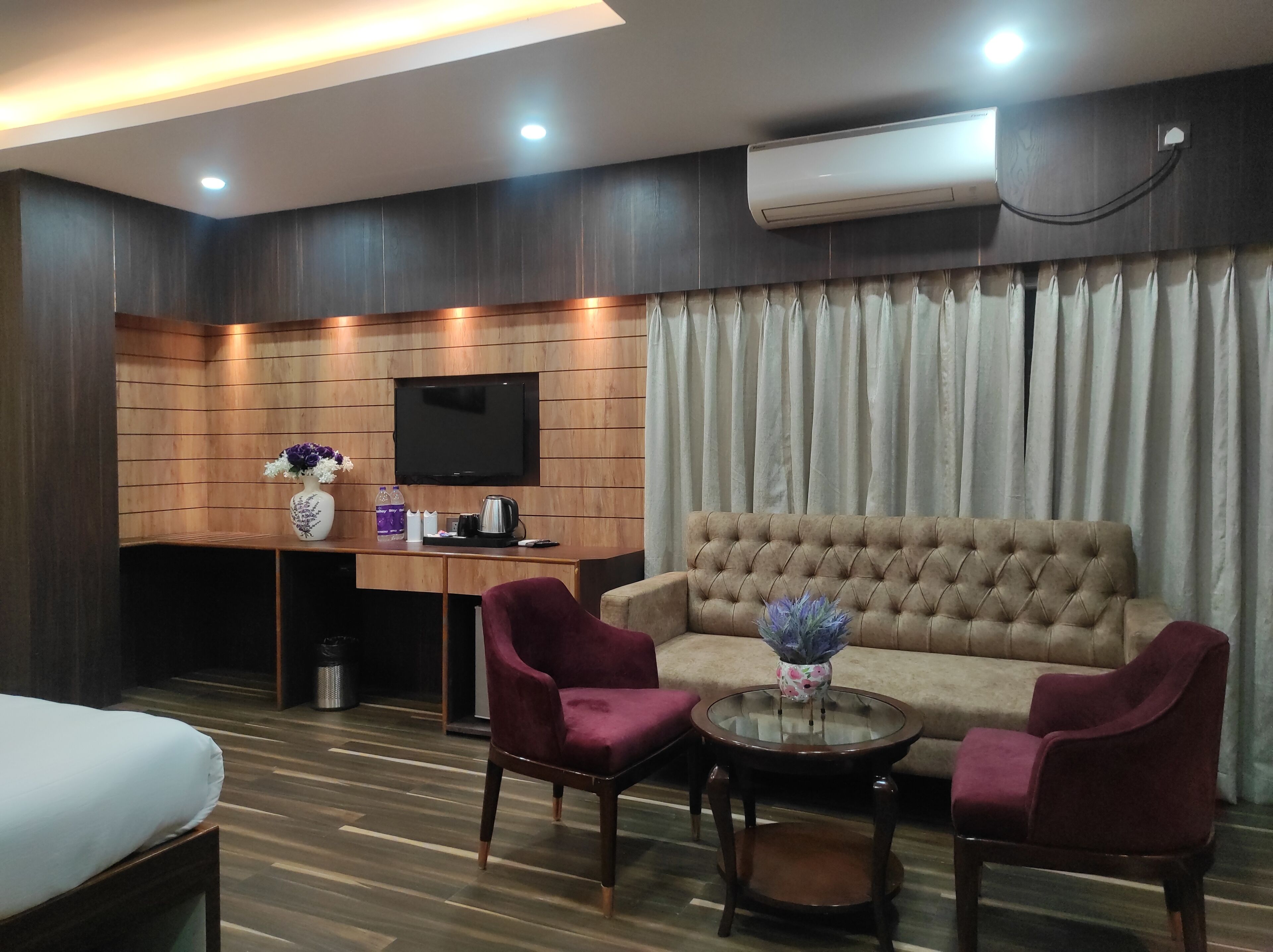 Una habitación de hotel moderna con un panel de pared de madera, un televisor de pantalla plana, un sofá, dos sillones, una mesa de centro y una cama.