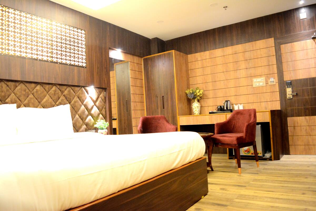 A hotel room with a large bed, a desk with a chair, and a wardrobe.