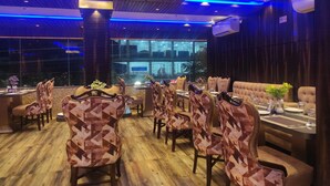 Un restaurante con una decoración moderna, que presenta sillas con diseños, suelo de madera y un amplio ventanal con vista a la ciudad.