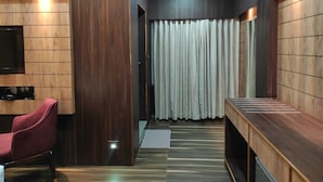 Una habitación de hotel moderna con un panel de pared de madera, un televisor de pantalla plana montado, una silla roja y un banco de madera.