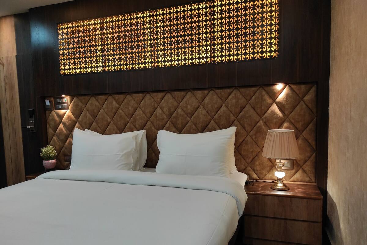 A hotel room with a large bed, a headboard with a geometric pattern, a bedside table with a lamp, and a decorative wall panel.