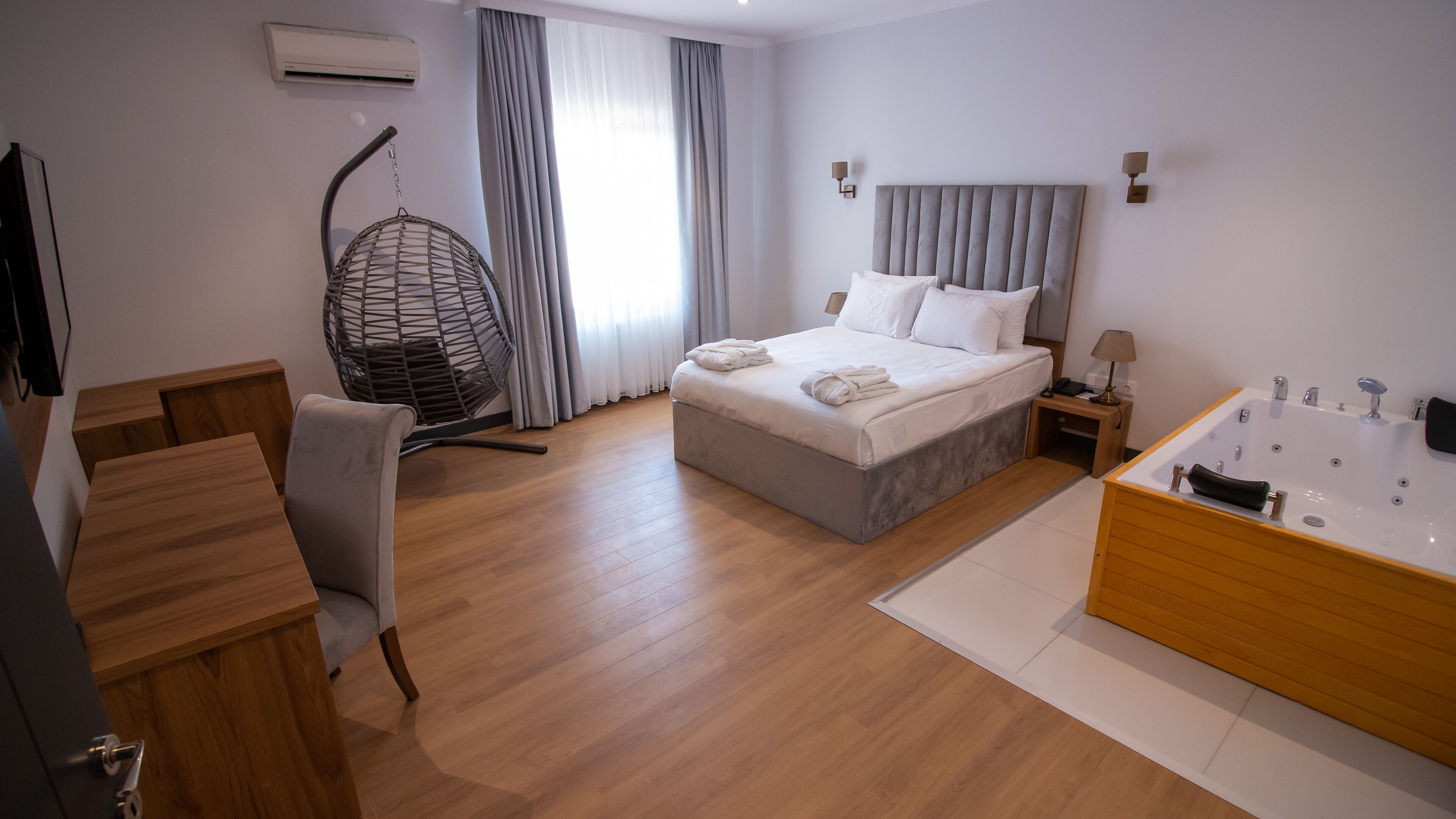 A modern hotel room with a bed, a sitting chair, a desk, a bathtub, and a hanging chair.