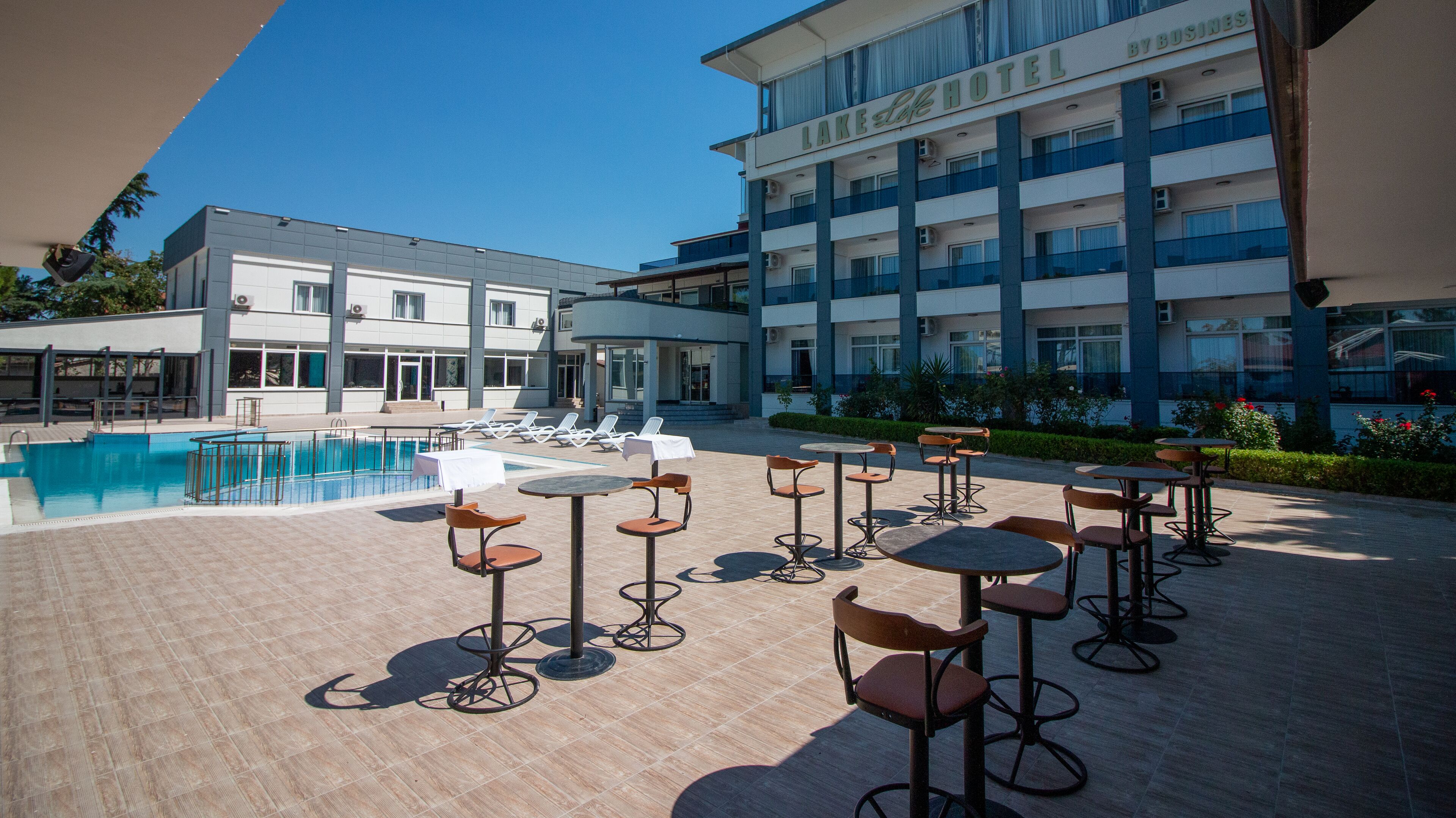 A hotel with a swimming pool, outdoor seating, and a multi-story building.