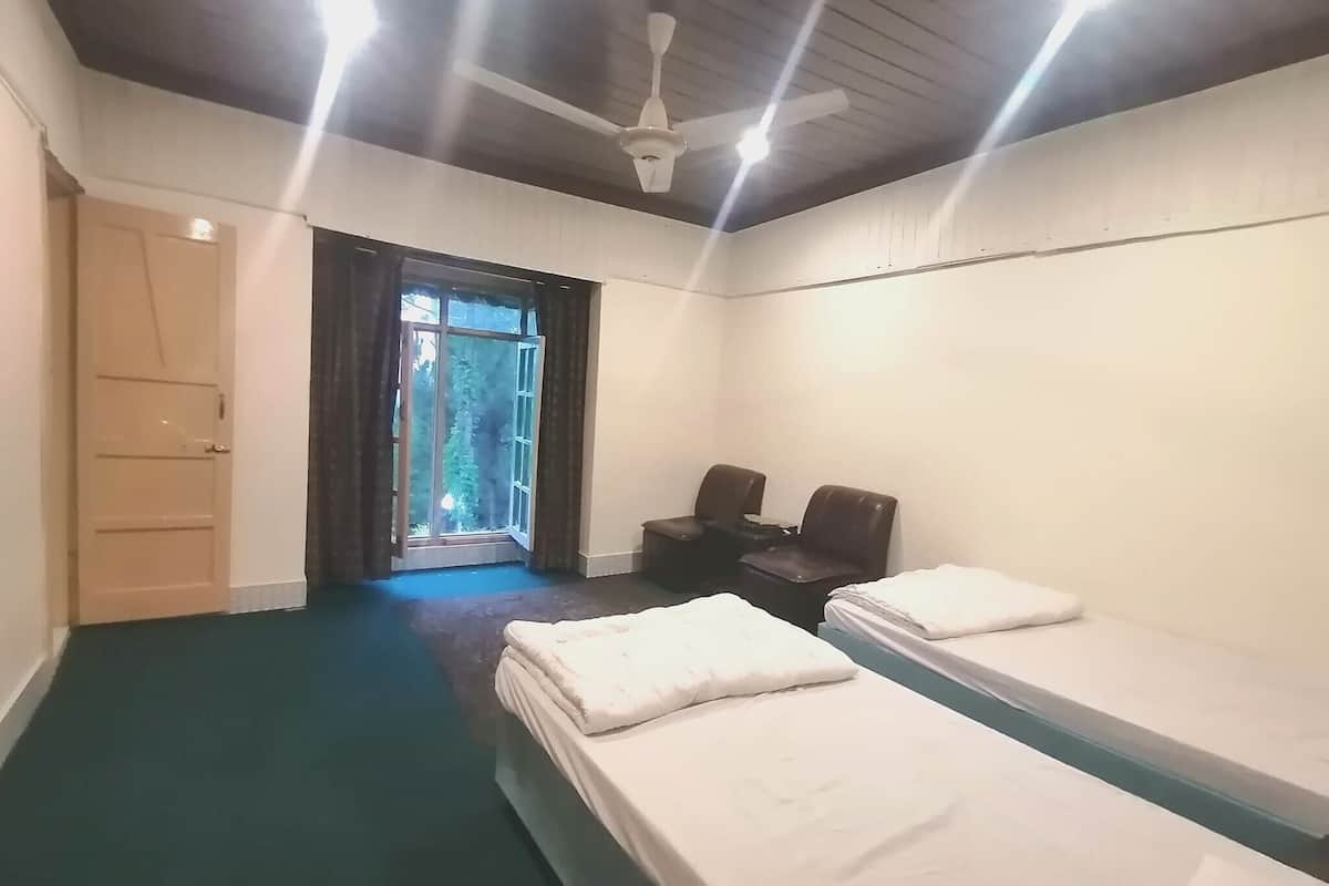 A room with two beds, a desk, a chair, and a ceiling fan.