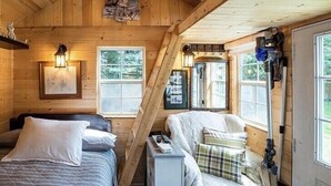 Een gezellig kamer in een blokhut met twee bedden, een klein tafeltje en een stoel. Er zijn ramen met gordijnen, een houten plafond en een deur.