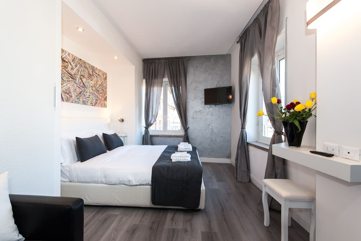 Ein modernes Schlafzimmer mit einem großen Bett, einem Nachttisch, einer kleinen Bank, einem Flachbildfernseher und einem Fenster mit Vorhängen.