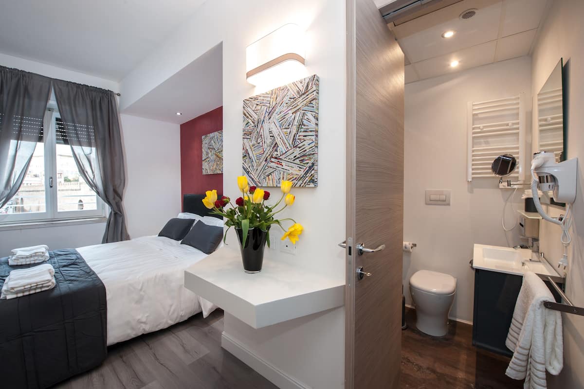 Ein modernes Hotelzimmer mit Bett, Nachttisch, Kunstwerk und einem Badezimmer mit Toilette und Waschbecken.