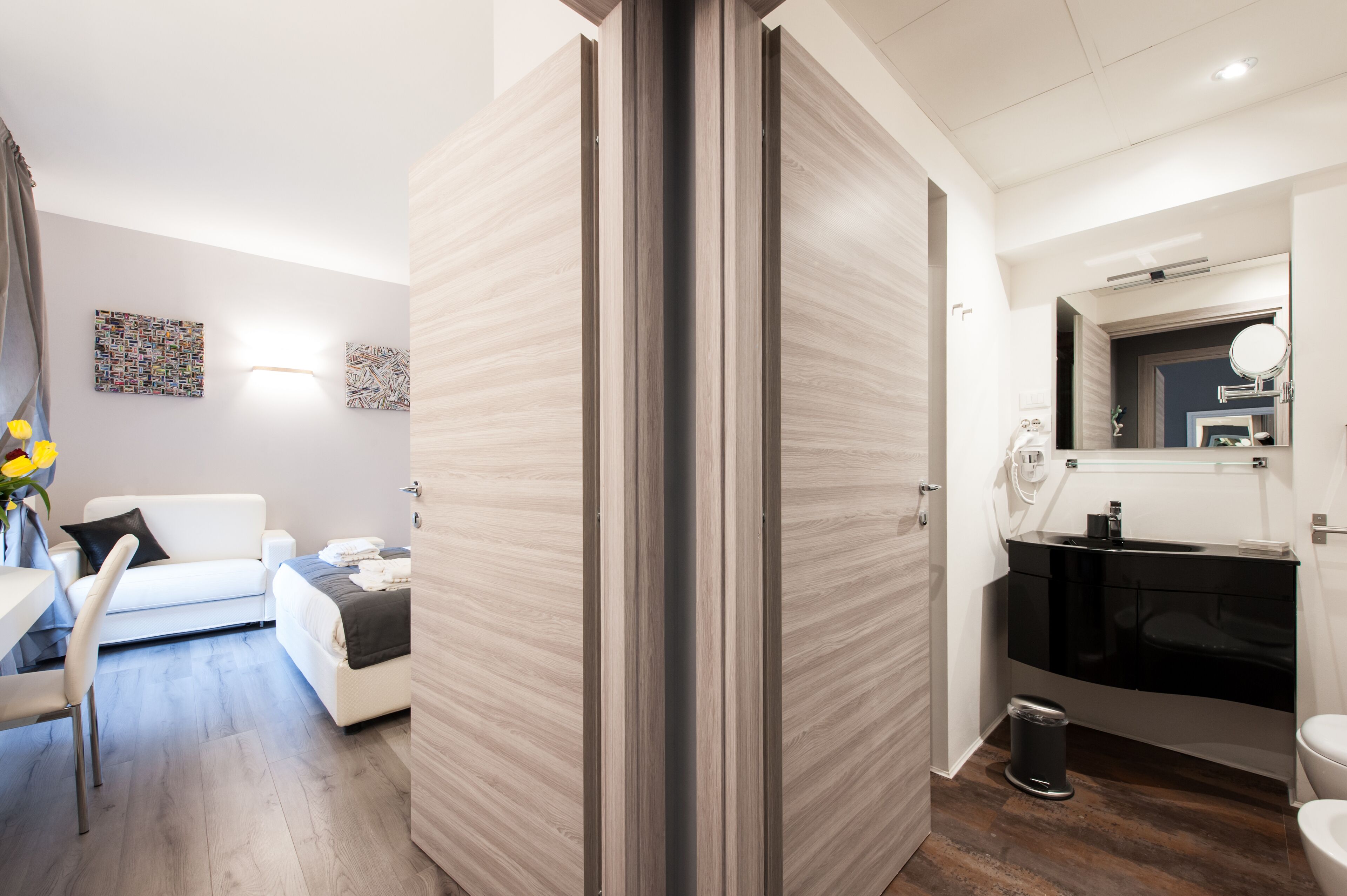 A modern hotel room with a white sofa, a dining table, and a large mirror in the bathroom.