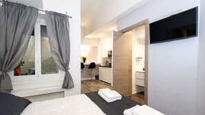 A modern hotel room with a bed, a TV mounted on the wall, and a view of the kitchen and bathroom. - Brunelleschi Holidays Hostel (Rome)
