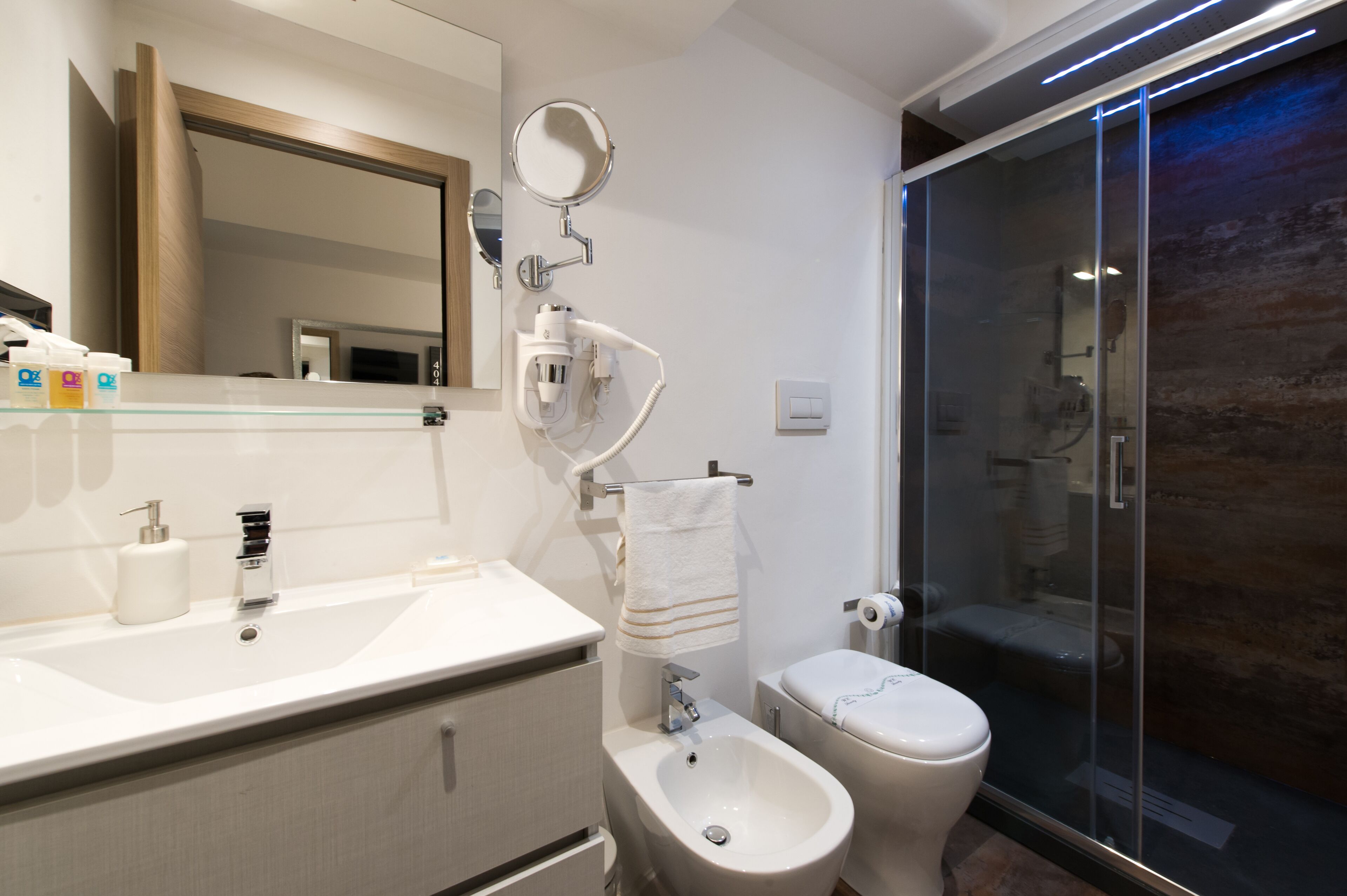 Une salle de bain moderne avec un grand miroir, un bidet, des toilettes et une douche à parois de verre.