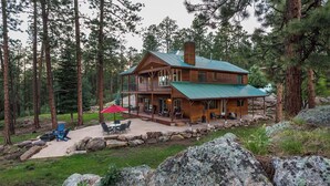 A two-story log cabin with a balcony, surrounded by a stone wall and a patio with outdoor furniture. - Luxury Home on 8 Acres - Fantastic Views and outdoor space - 20 Min to DGO (Durango)