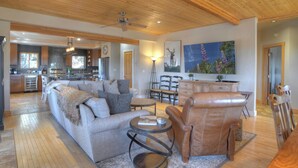 A spacious living room with a grey sofa, a leather armchair, and a dining area with a wooden table and chairs. - Luxury Home on 8 Acres - Fantastic Views and outdoor space - 20 Min to DGO (Durango)