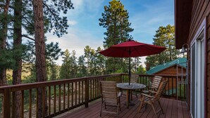 A wooden deck with a red umbrella, two wooden chairs, and a small round table.