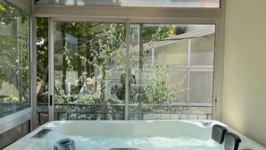 A hot tub in a sunlit room with large windows and a view of a backyard. - Magnifique Maison Avec Jacuzzi (Marseille)