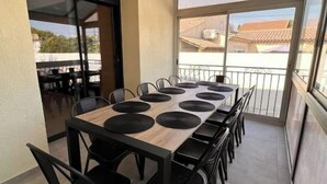 A covered outdoor dining area with a long table and chairs, large windows, and a view of the neighborhood. - Magnifique Maison Avec Jacuzzi (Marseille)