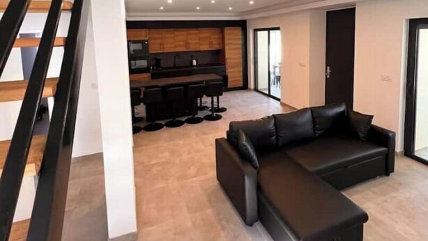 A modern living room with a sectional sofa, a kitchen area, and a staircase. - Magnifique Maison Avec Jacuzzi (Marseille)