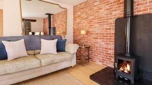 A living room with a brick wall, a sofa with cushions, a mirror, a lamp, and a wood-burning stove. - Baa Lamb Cottage (Romney Marsh)