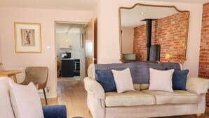 A living room with a sofa, a chair, a coffee table, and a kitchen in the background. - Baa Lamb Cottage (Romney Marsh)