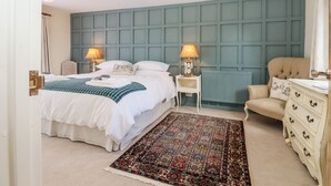 A bedroom with a large bed, two bedside tables with lamps, a chair, a dresser, and a patterned rug. - Baa Lamb Cottage (Romney Marsh)