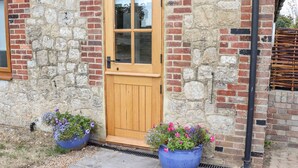 A stone building with a wooden door and two flower pots on the ground. - Baa Lamb Cottage (Romney Marsh)