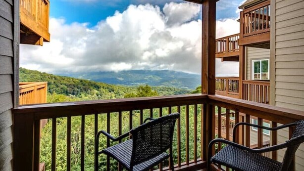 A balcony with two wicker chairs, wooden railings, and a view of a mountainous landscape under a partly cloudy sky. - Suite Spot at Sugar-Mountain Views (Sugar Mountain)