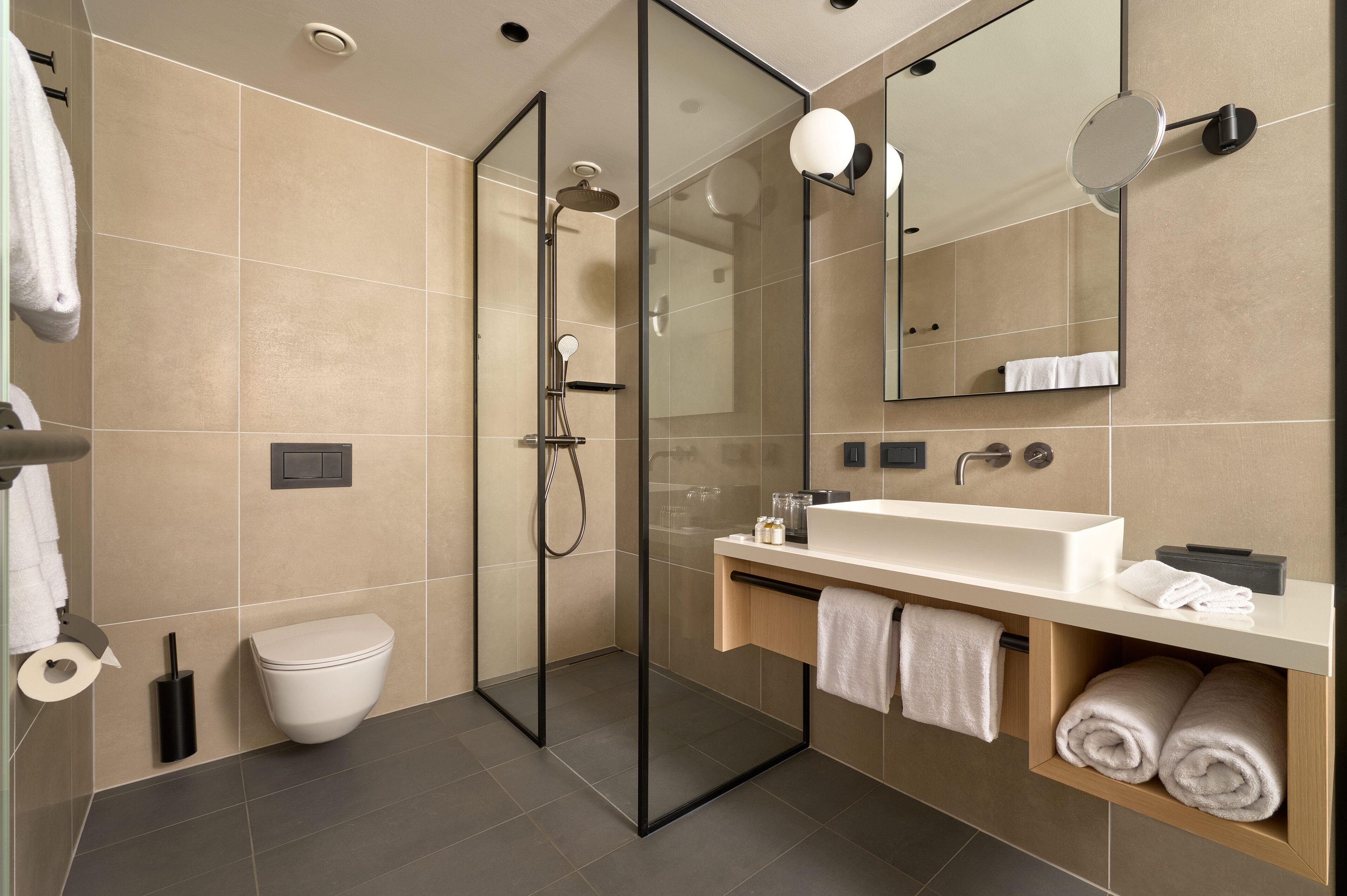 Een moderne badkamer met een douche met glazen wand, een wit toilet, een groot wastafelmeubel met spiegel en een handdoekrek.