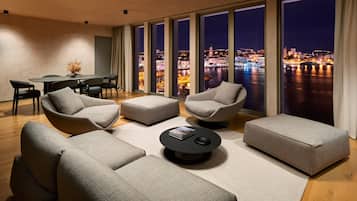 Una sala de estar moderna con vista a la ciudad, que incluye un juego de sofás, una mesa de centro y un comedor con sillas y una mesa.