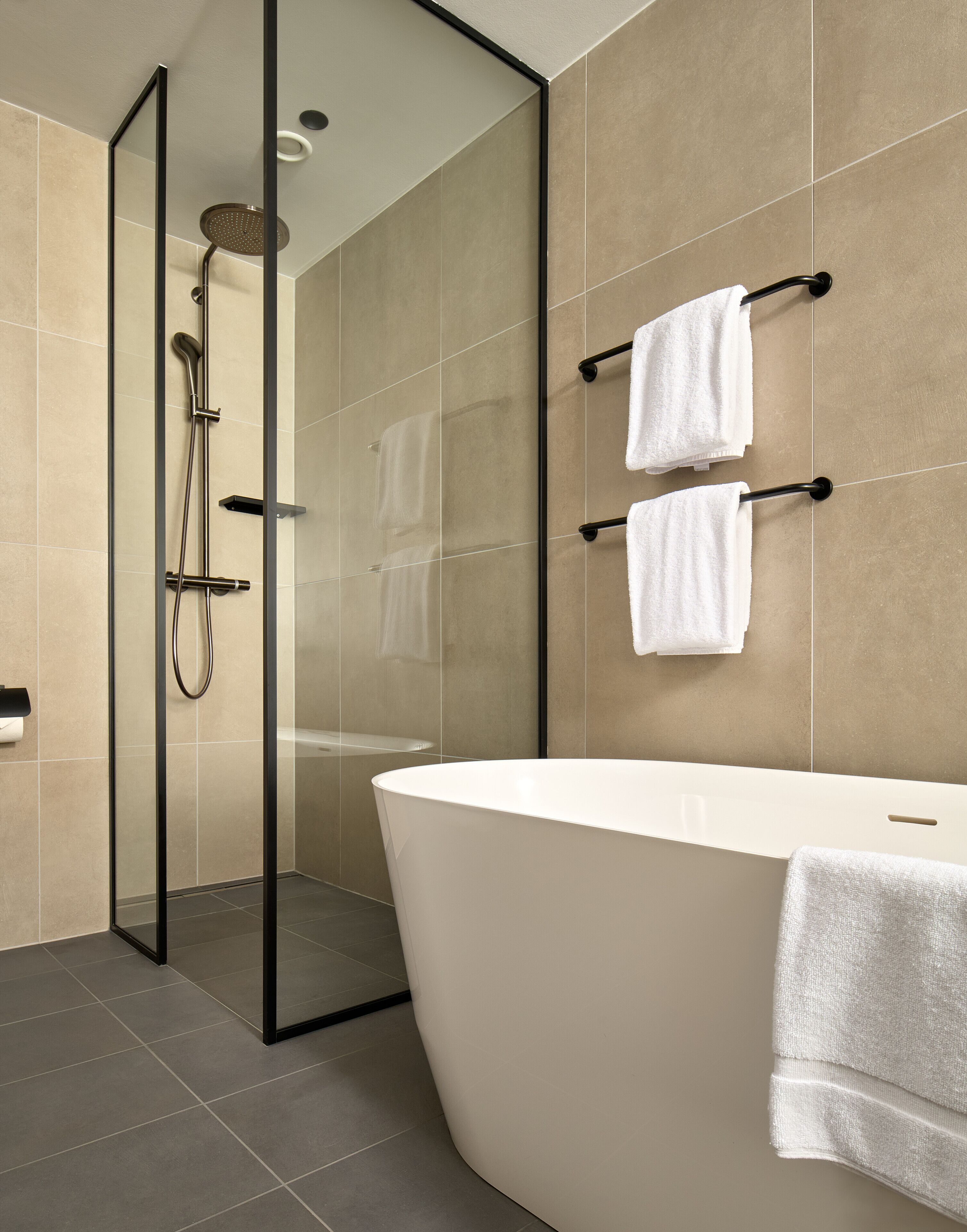A modern bathroom with a freestanding bathtub, a glass-enclosed shower area, and two towels hanging on a towel rack.