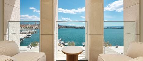 Un balcón con una mesa de madera y dos sofás color beige, con vista a un cuerpo de agua con barcos y un paisaje urbano distante.