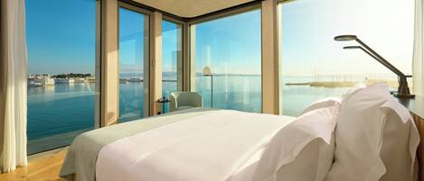 A modern hotel room with a large bed, a desk, and a view of the sea.
