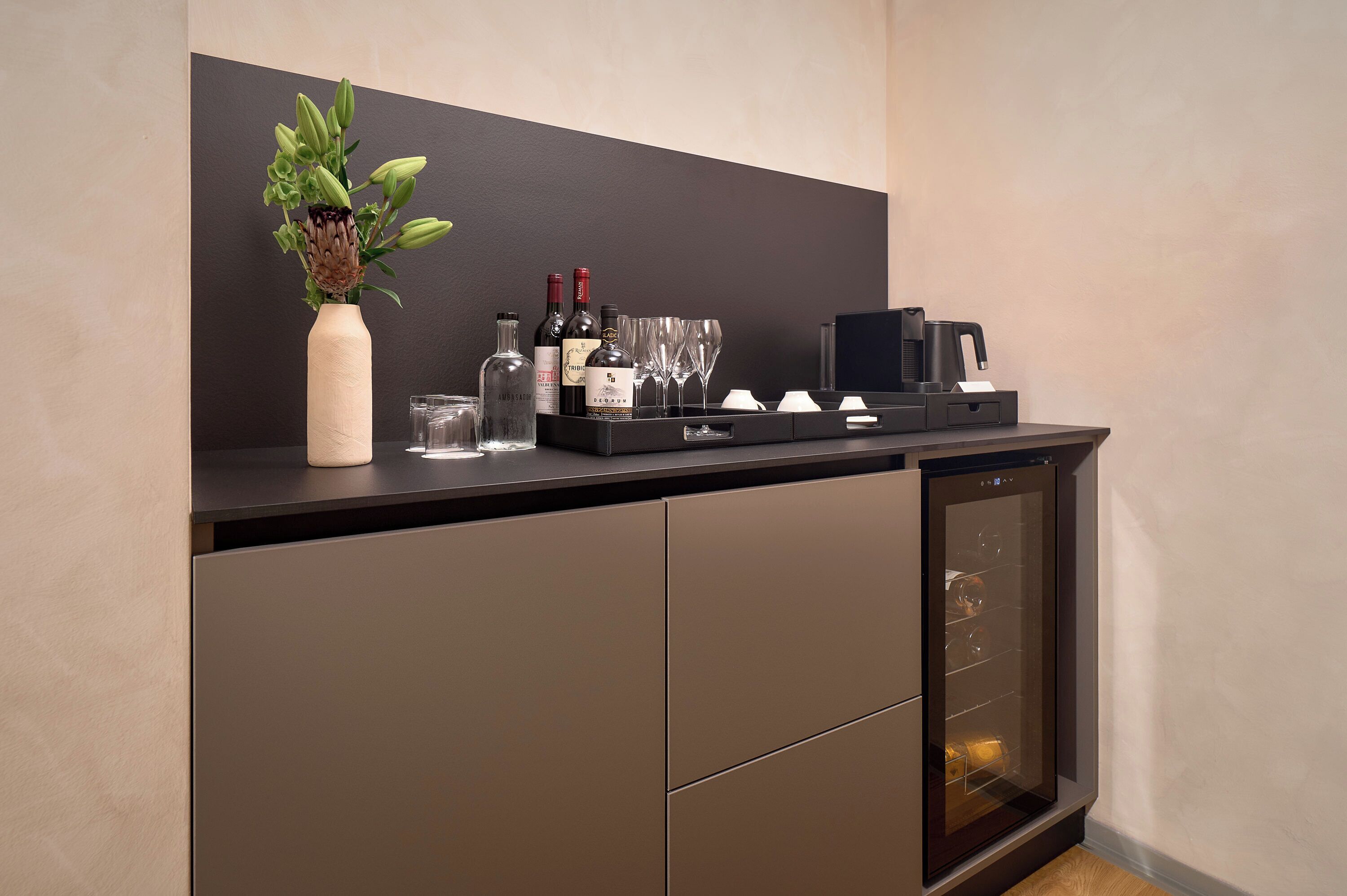 A modern bar area with a wine bottle, glasses, and a coffee machine.
