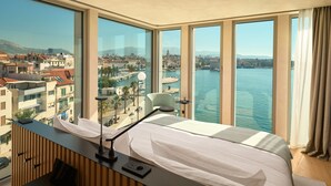 Een hotelkamer met een groot raam, met uitzicht op een stad en een wateroppervlak.