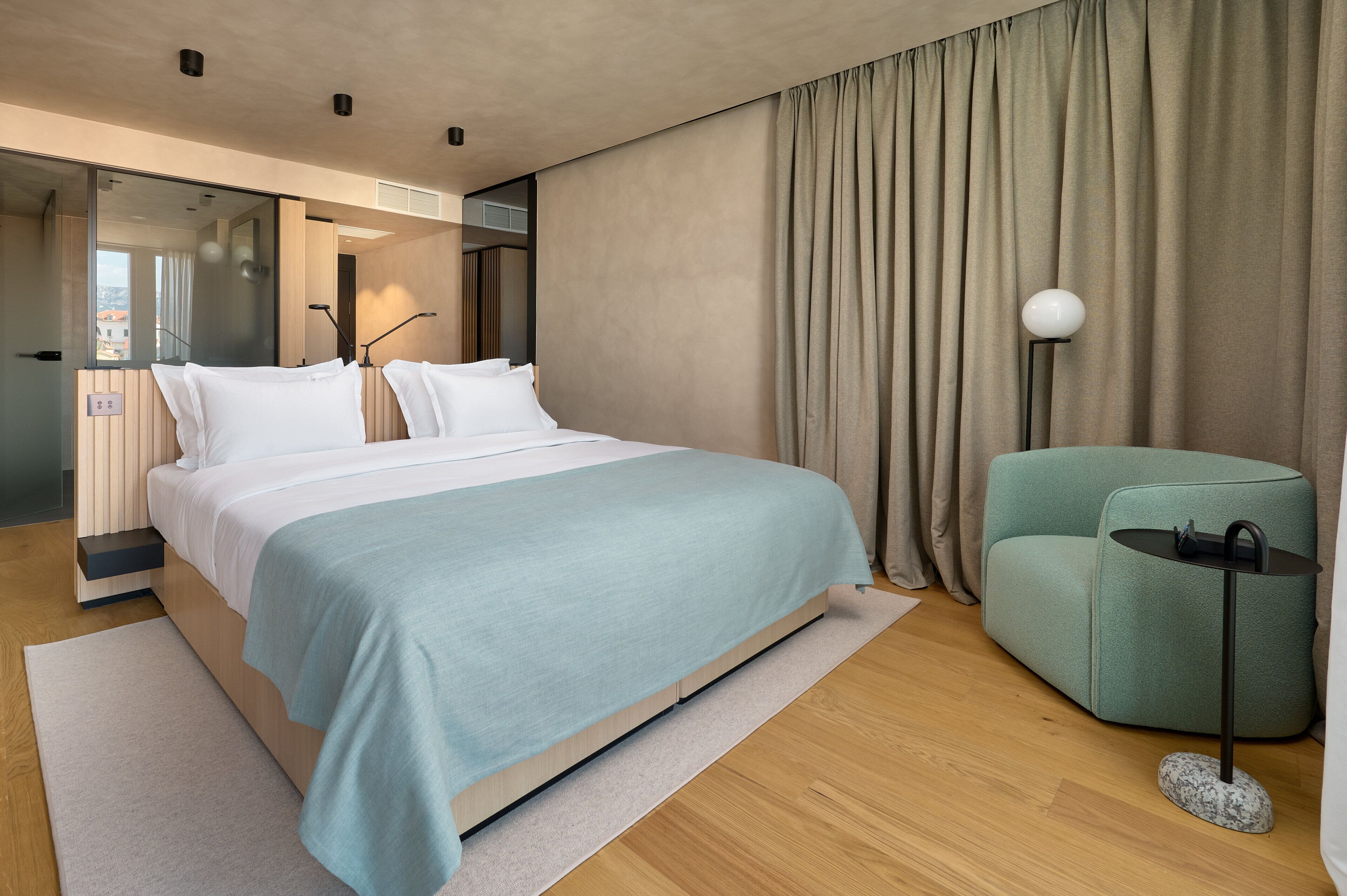 A modern hotel room with a large bed, a seating area, and a view through a glass door.